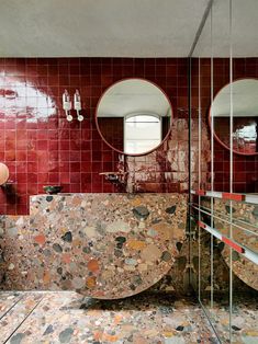 a bathroom with two sinks and mirrors on the wall next to each other in front of a red tiled wall