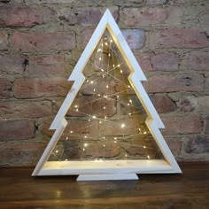 a small wooden christmas tree with lights on it's sides, against a brick wall