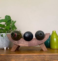 three wine bottles sitting on top of a wooden stand next to two vases and a potted plant