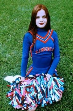 a young woman sitting on the grass wearing a cheerleader outfit and posing for a photo