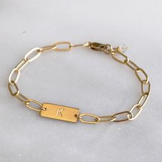 This stunning personalized bracelet is meaningful and stylish. This dainty bracelet is handmade with silver or gold chain and your initial or symbol. It makes a wonderful gift for her for any occasion. D E T A I L S *Thick 16mm bar *Paperclip chain *100% 14kt Gold-Filled JUST FOR YOU *Stamped by hand with an initial in classic block. *See our chart for available symbols. *Satin finish. LENGTH Fits most sizing: 6.0 inches extra small 6.5 inches small 7.0 inches medium 7.5 inches large HOW TO PERS Stamp Bracelet Ideas, Personalized Gold Metal Bracelets, Simple Personalized Jewelry For Friendship, Personalized Simple Jewelry For Friendship, Modern Metal Chain Bracelet Personalized, Classic Personalized Metal Chain Bracelet, Everyday Stainless Steel Nameplate Jewelry, Gold Sterling Silver Paperclip Bracelet For Everyday, Personalized Gold Bracelets With Rectangular Links