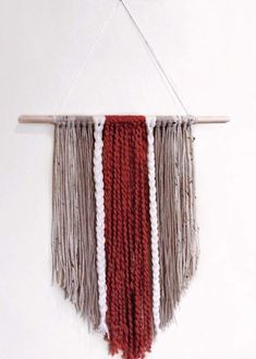 a red and white wall hanging with fringes on it's side, in front of a white wall