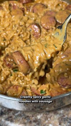 a spoon full of food that is being held by someone's hand with the words creamy spicy garlic noodles with sausage on it