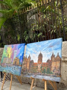 three easels with paintings on them in front of a fence