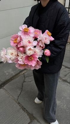 a man holding a bouquet of flowers on the street with his cell phone showing it