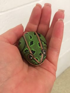 a hand holding a green frog brooch with hearts on it's face and eyes