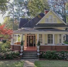 a small yellow house with white trim and red front door, surrounded by trees and flowers