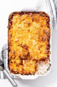 a casserole dish with meat and cheese in it on a towel next to utensils