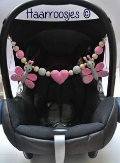 a baby car seat with pink and grey decorations on it's back end, in front of a sign that says harroosee