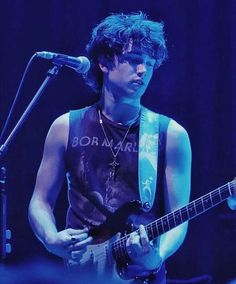 a young man playing an electric guitar in front of a microphone