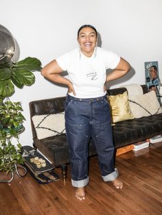 a woman standing in front of a couch with her hands on her hips and smiling