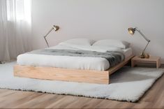 a bed sitting on top of a white rug next to a wooden table and lamp