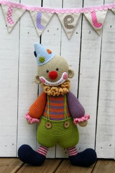 a crocheted stuffed animal wearing a party hat and overalls, standing in front of a wooden fence