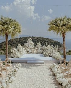 an outdoor wedding setup with white flowers and palm trees in the foreground, surrounded by clear blue water