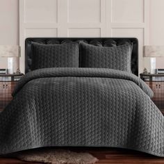 a bed with grey bedspread and pillows on top of wooden floor next to white wall