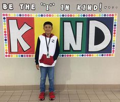 a young boy standing in front of a sign that says be the i'm kind