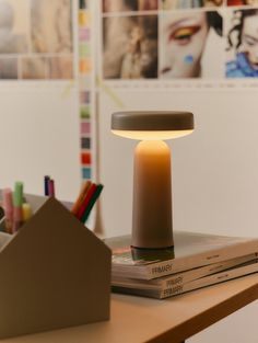 a lamp sitting on top of a wooden table next to books and pencils in front of pictures