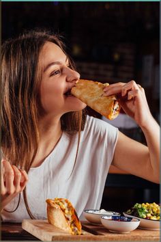 a woman sitting at a table eating a piece of food with her mouth wide open