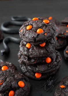 chocolate cookies with orange candies are stacked on top of each other in front of a black background