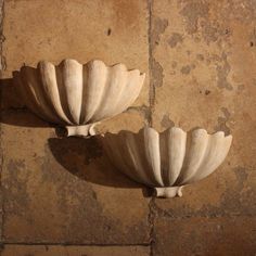 two white scallop shaped vases sitting on top of a stone floor