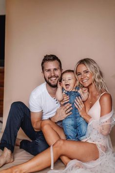 a man, woman and baby are sitting on the bed together smiling at the camera