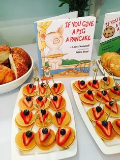 two plates with croissants and strawberries on them next to a book