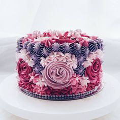 a pink and purple cake with flowers on it sitting on a white platter in front of a white backdrop