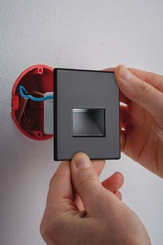 a person is holding an electrical device in their hand and pressing the button on the wall