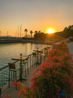 the sun is setting over some water with tables and chairs