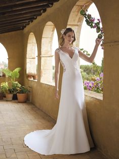 a woman in a white wedding dress leaning against a wall with her hand on the flower