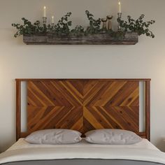 a wooden headboard with candles above it in a white bedroom, next to two nightstands