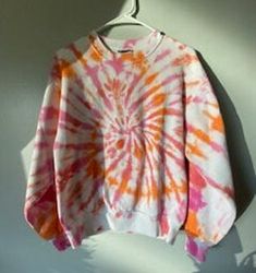 an orange, pink and white tie - dyed sweater hanging on a hanger against a wall