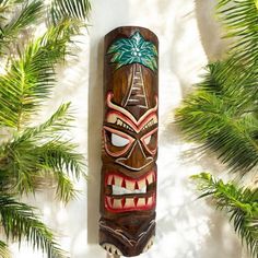 a tiki mask hanging from the side of a wall next to some palm trees