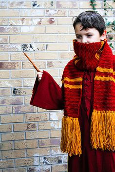 a young boy dressed in red and yellow holding a stick while standing next to a brick wall