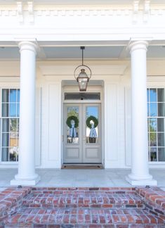 the front entrance to a white house with two wreaths on it's pillars