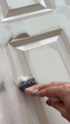 a person holding a paint brush in front of a door with white paint on it