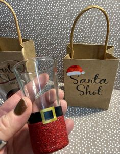 a hand holding a small glass with santa hat on it next to a brown paper bag