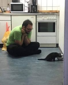 a man sitting on the floor next to a cat