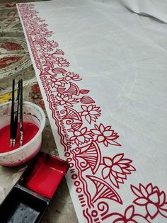 the table is covered with red paint and has black brushes in it next to a bowl of water