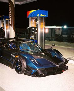 a black sports car parked in front of a gas station at night with no one around