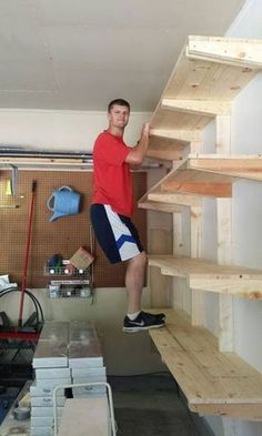 a man standing on top of a wooden shelf next to shelves filled with wood planks