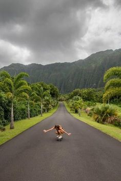 a woman riding a skateboard down the middle of a road next to palm trees