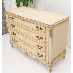 an old dresser is painted white and has gold hardware on the drawer pulls, along with a potted plant