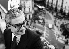 black and white photograph of a man in glasses looking down at the street below him