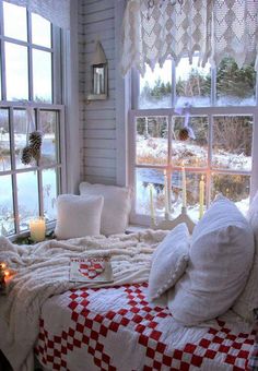 a bed sitting next to a window in a room filled with pillows and blankets on top of it