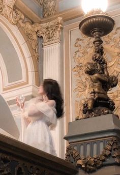 a woman in white dress standing on top of a balcony next to a light fixture