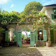 a house with green shutters on the front and side doors open to let in light