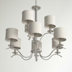 a white chandelier with six lamps hanging from it's sides and four shades off to the side