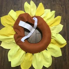 a sunflower wreath made out of felt and white ribbon on a wooden floor with a piece of paper taped to it