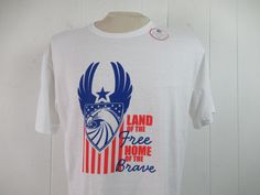 "Vintage 1990s or 2000s t-shirt. Made of white cotton with red, white and blue patriotic graphics. Reads: Land of the free home of the brave. Has U.S. Air Force style logo. Size large. Actual measurements are: 44\" around the chest 44\" around the waist 19.5\" shoulder seam to shoulder seam 29\" overall length In excellent unused condition. New old stock." Red Americana T-shirt With American Flag, Made In Usa Crew Neck T-shirt For Veterans Day, White Americana Letter Print T-shirt, White Flag Print T-shirt For Streetwear, American Style Pre-shrunk Cotton T-shirt, White Cotton T-shirt With American Flag Print, Americana Style Relaxed Fit Short Sleeve T-shirt, White American Flag T-shirt For Independence Day, Patriotic 4th Of July Streetwear T-shirt